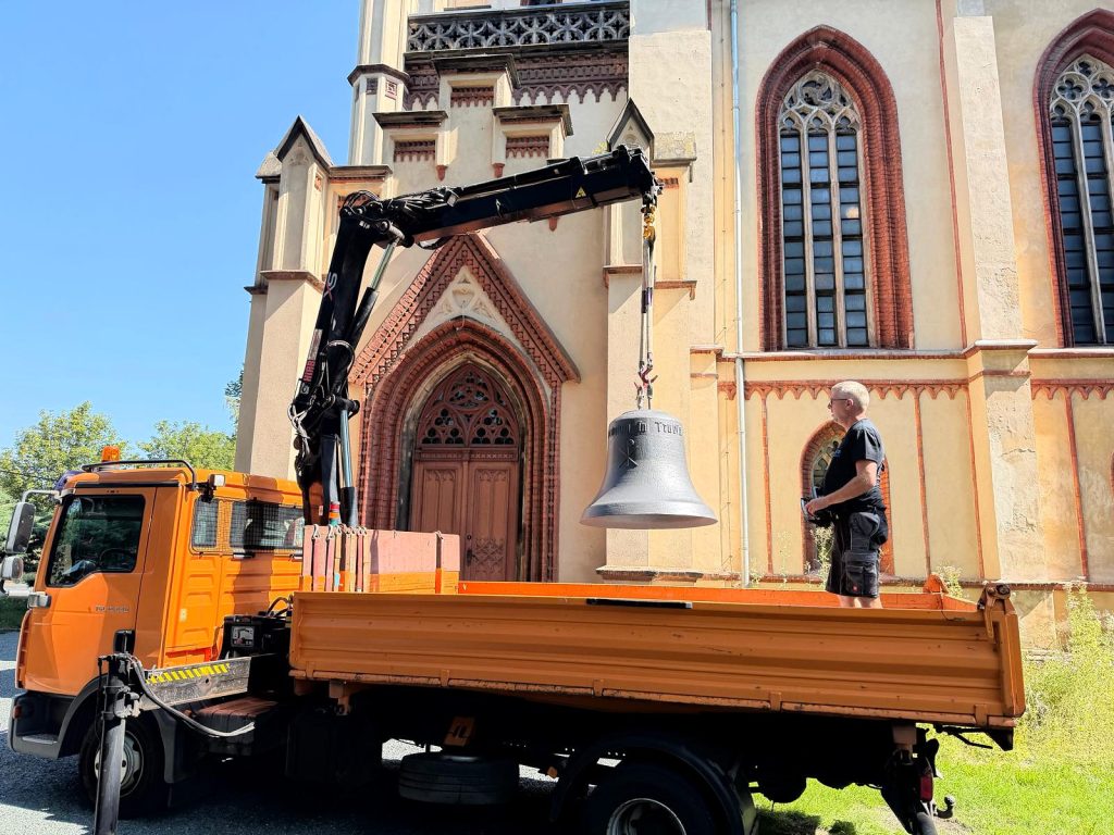 Ein Ladekran hebt die Glocke über die Ladefläche eines Lastwagens vor der Kirche